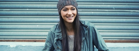 Smiling woman with black smooth hair with softness leaning on a wall.