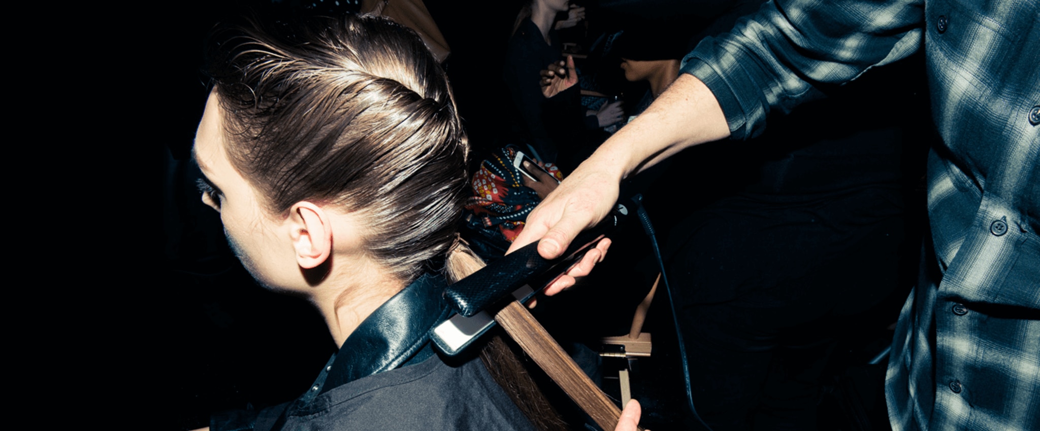 Backstage at a fashion show, a stylist straightens a model's long brown hair