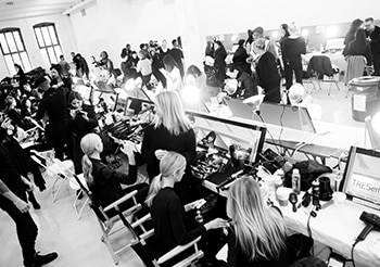 Model-model sedang duduk di depan cermin dengan para penata rambut, fotografer, alat-alat dan produk-produk penataan rambut 