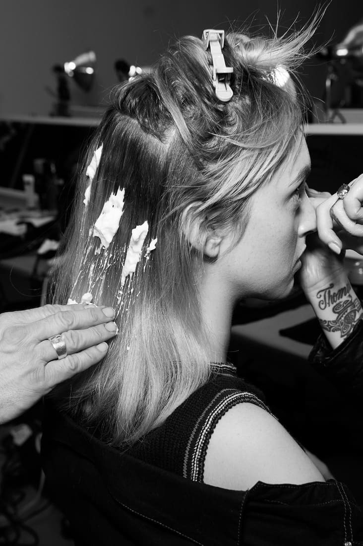 A model's blonde hair up in clips and a stylist blow drying it with a large brush
