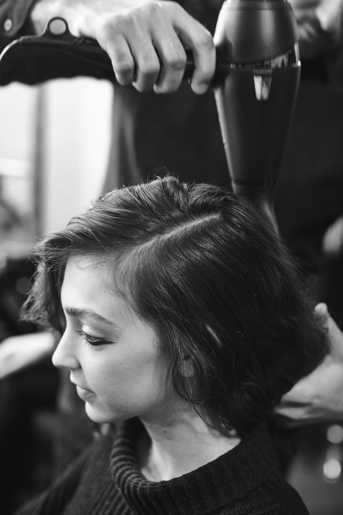 Uma modelo sentada com seu cabelo partido e um cabeleireiro usando um secador no cabelo dela