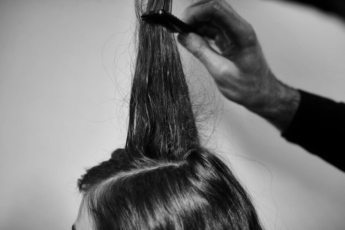 Um cabeleireiro levantando um segmento do cabelo de uma modelo e penteando-o para trás