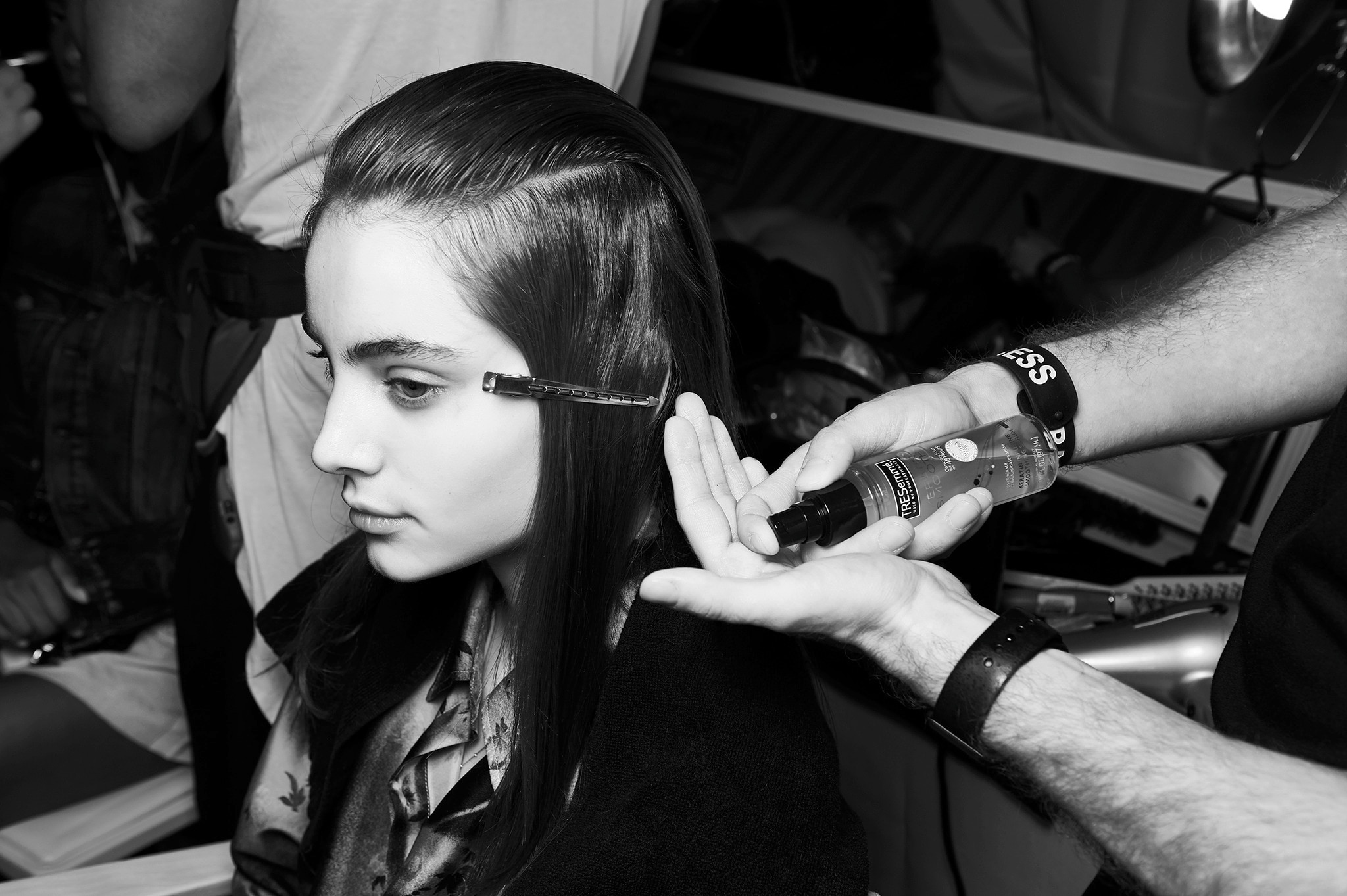 A model with her hair held in place with a clip, and a stylist applying product to it
