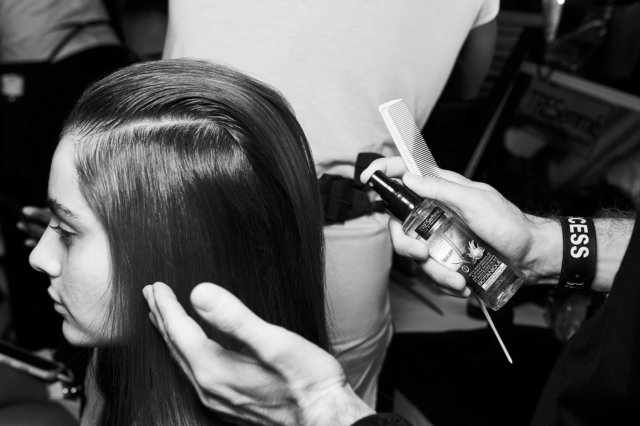 Las manos de un estilista uniendo secciones del cabello de una modelo con la ayuda de un pasador.