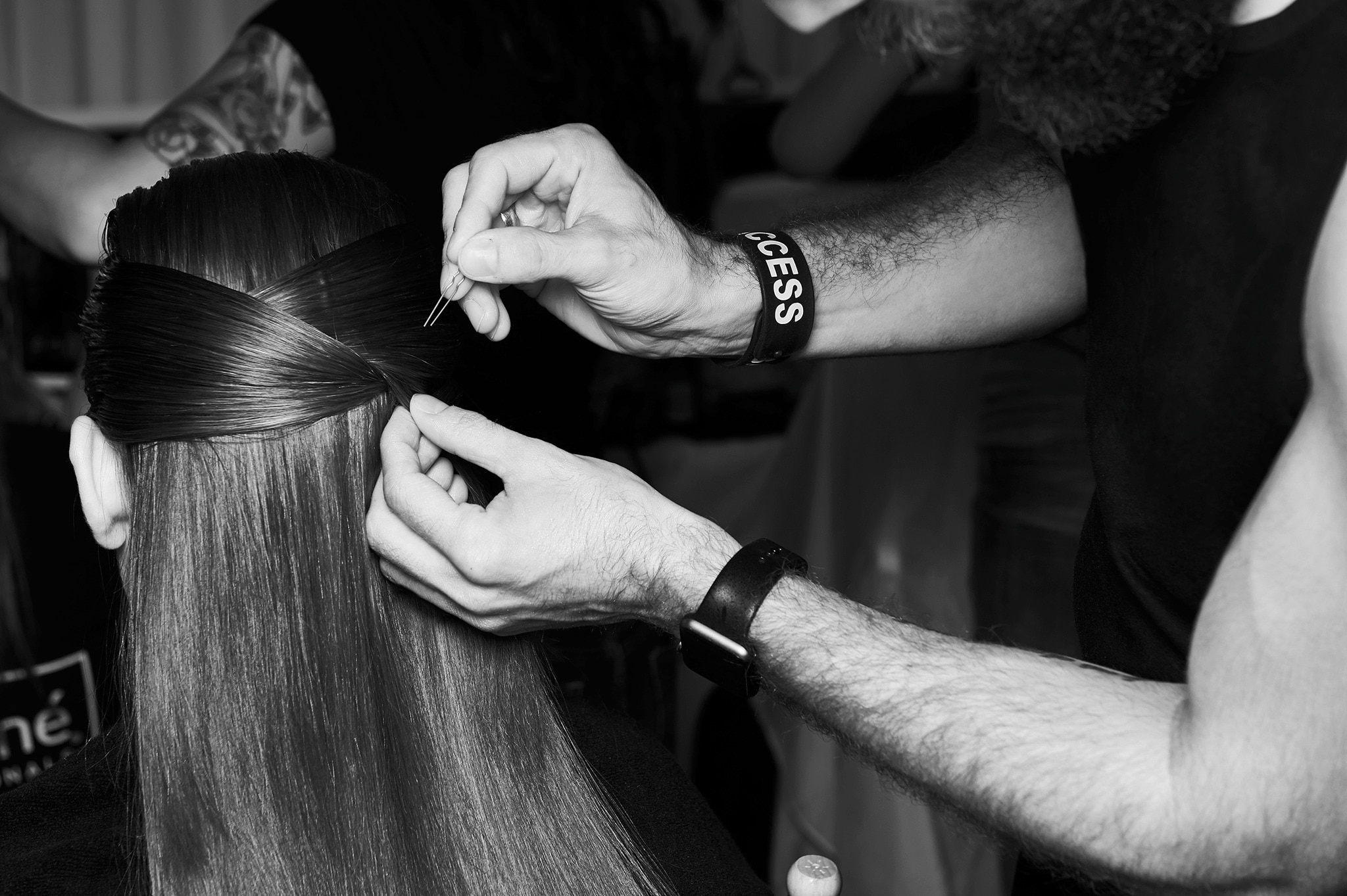 A stylist's hands tying sections of a model's hair together with the help of a bobby pin