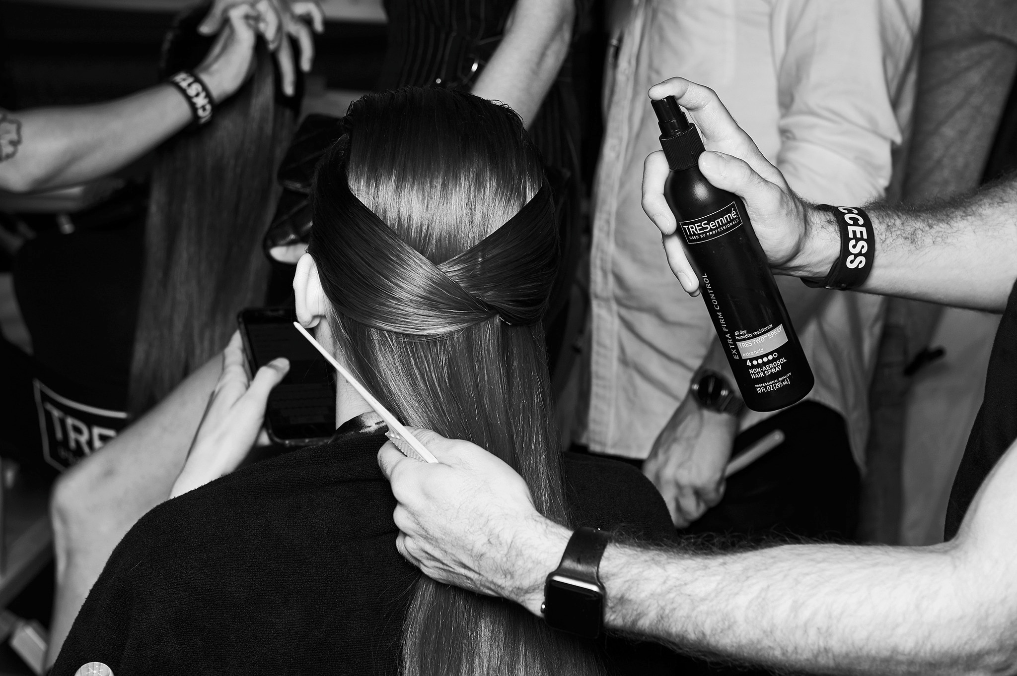 A stylist applying spray to a model's hair with other models and stylists in the background