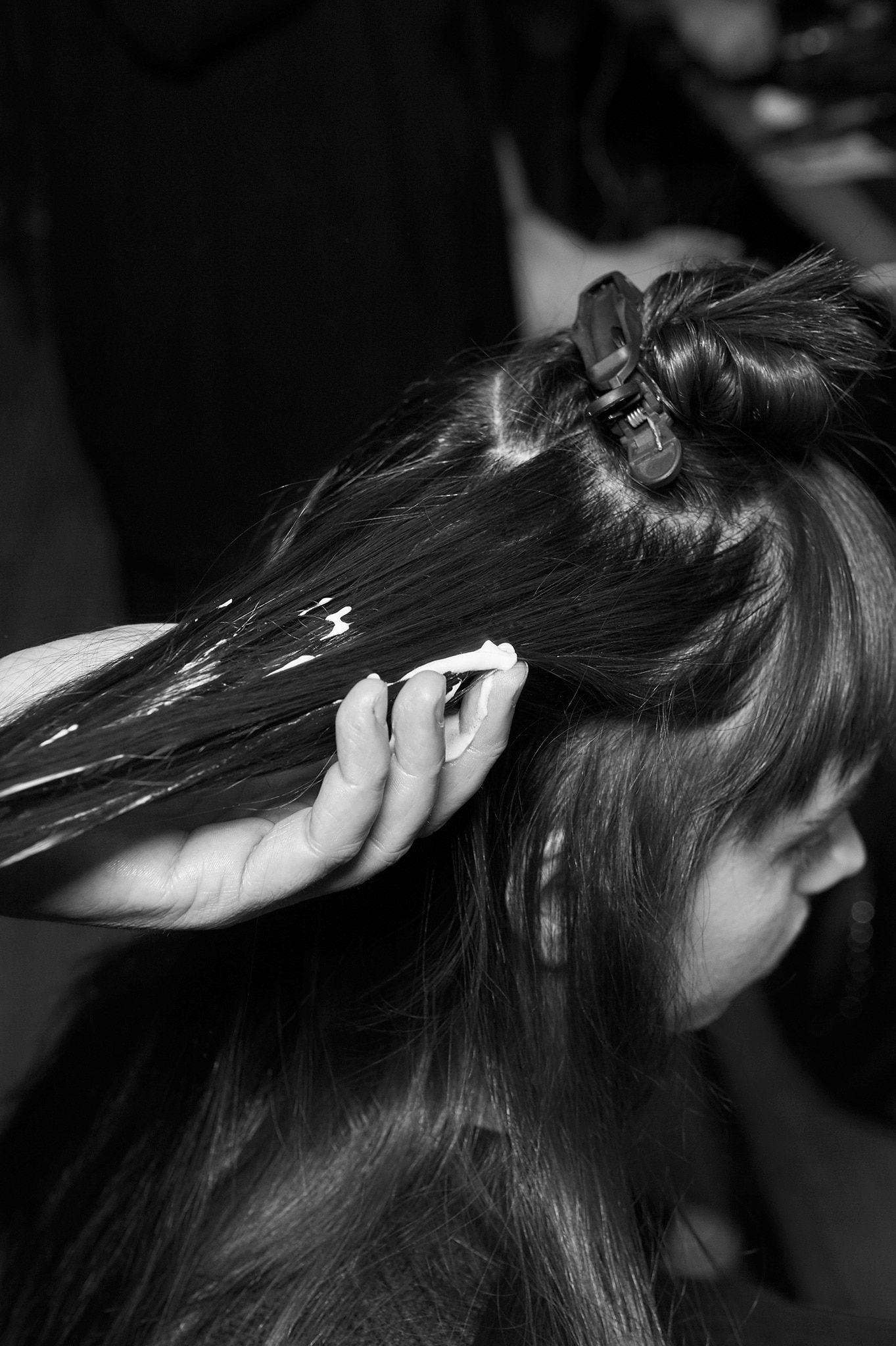 A model with her hair in a clip and a stylist's hands appling mousse to a section of it