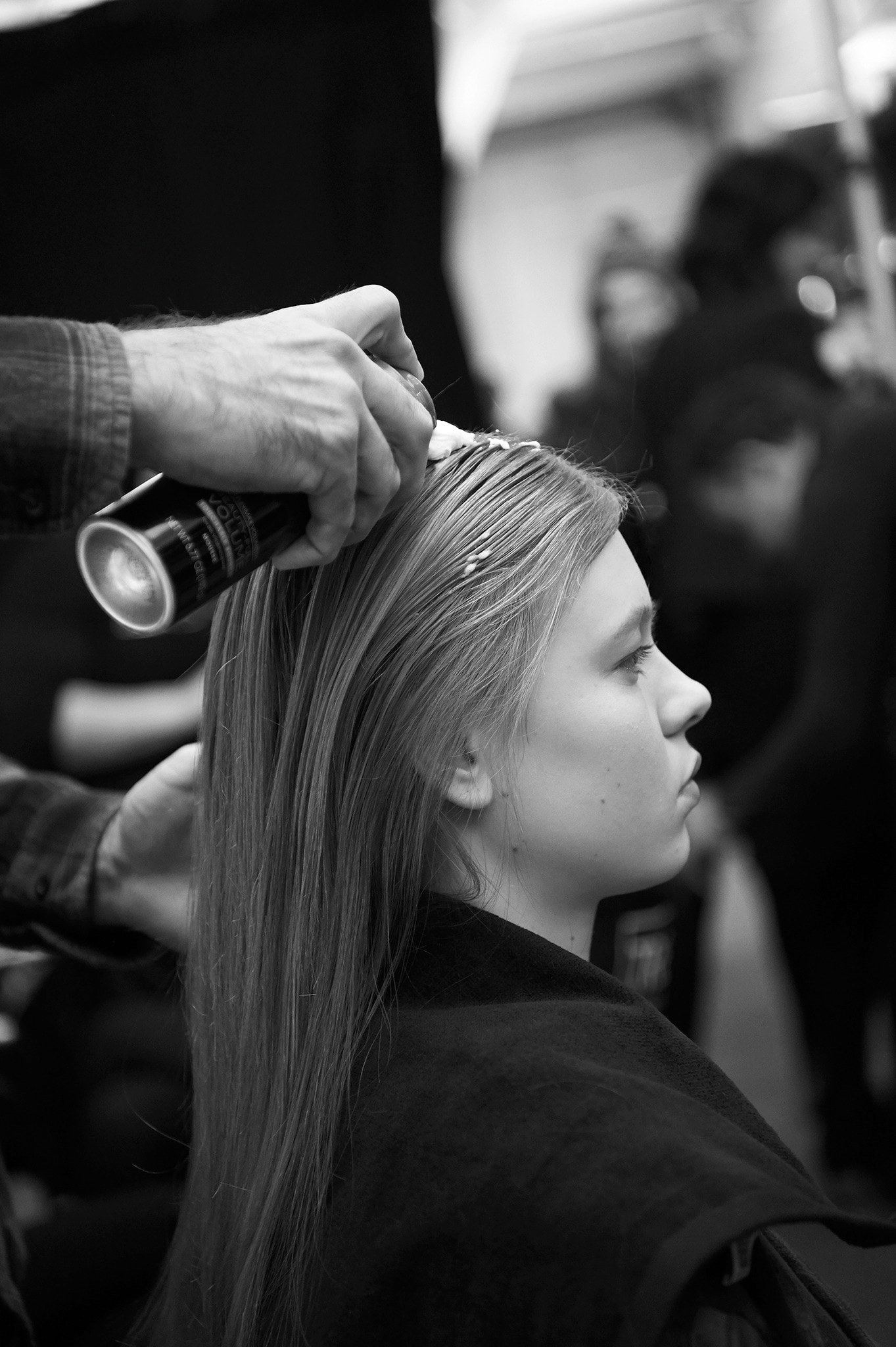 A blonde model's head and shoulders, with a stylist's applying mousse to it