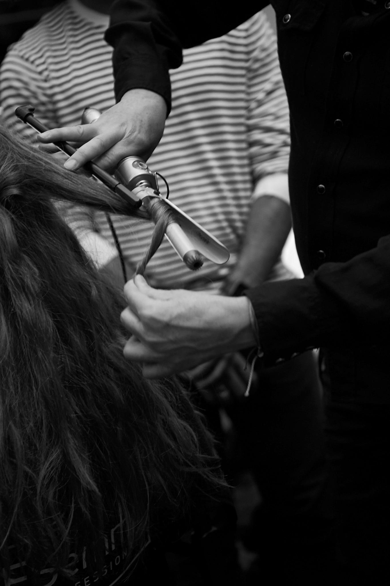 A stylist using curling tongs on a model's long, dark curly hair