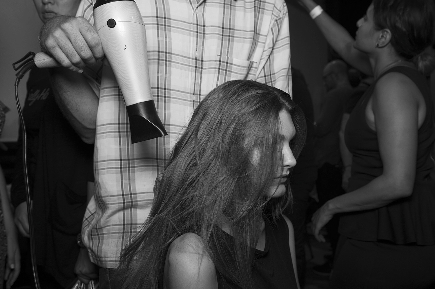 Un estilista sosteniendo un secador,   secando un tramo de pelo húmedo de una modelo