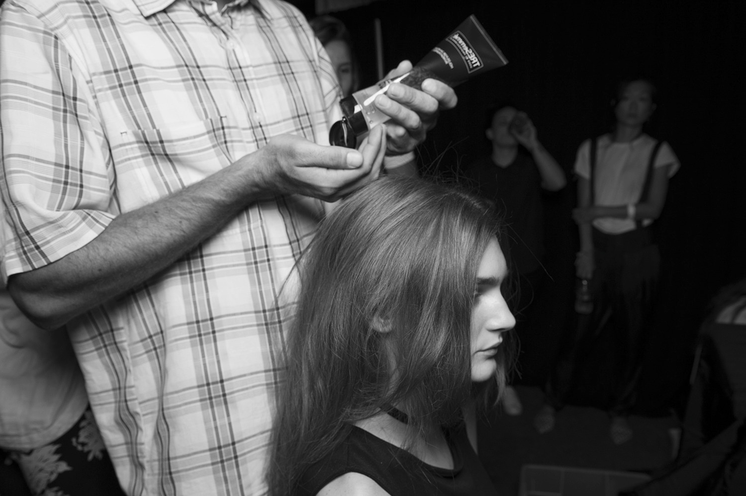 Un estilista sosteniendo un tubo de producto y apretándolo con sus manos listo para aplicarlo en el pelo de una modelo