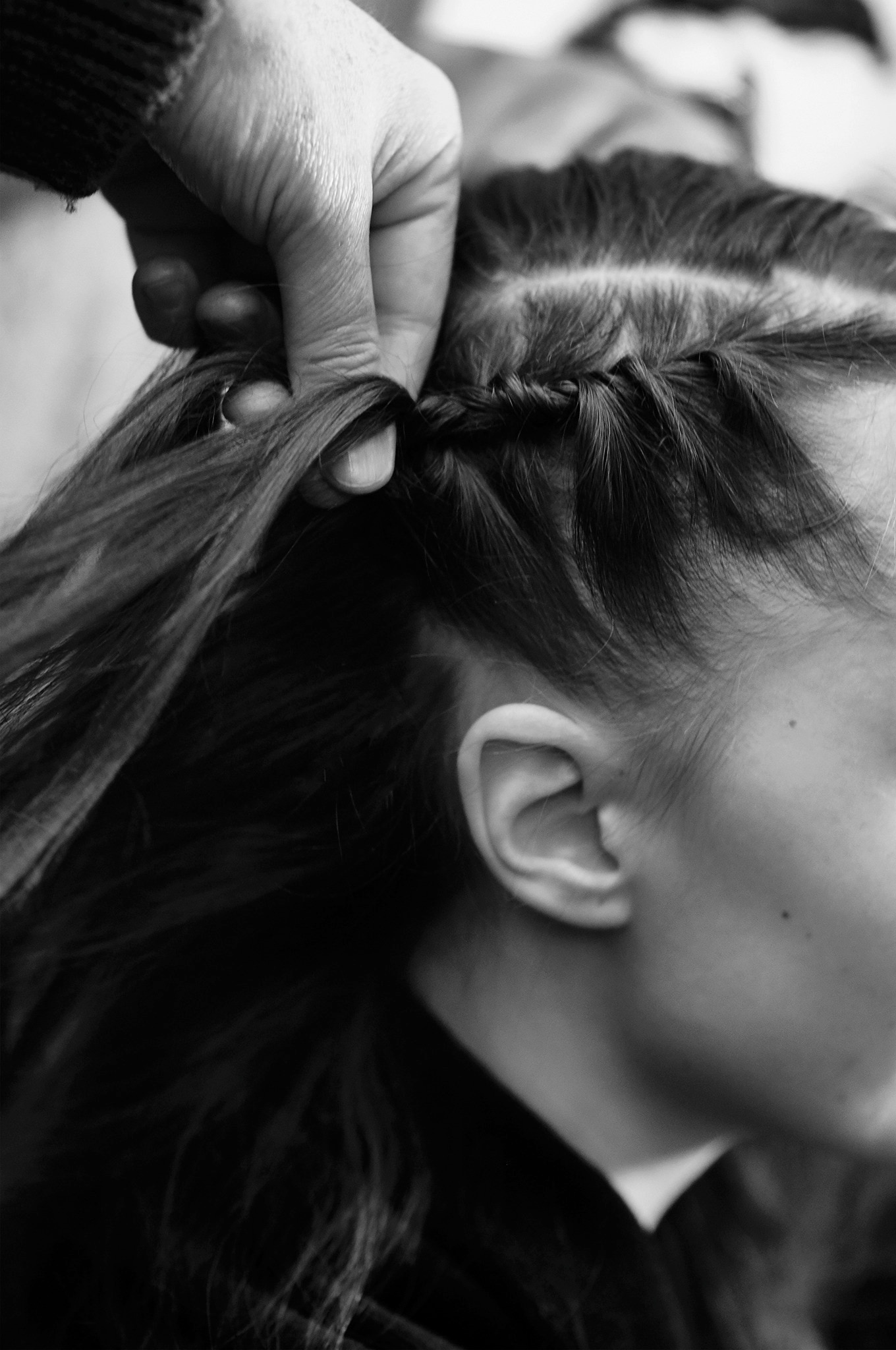 Someone's hands fastening a model's long, dark wavy hair into tight braids.