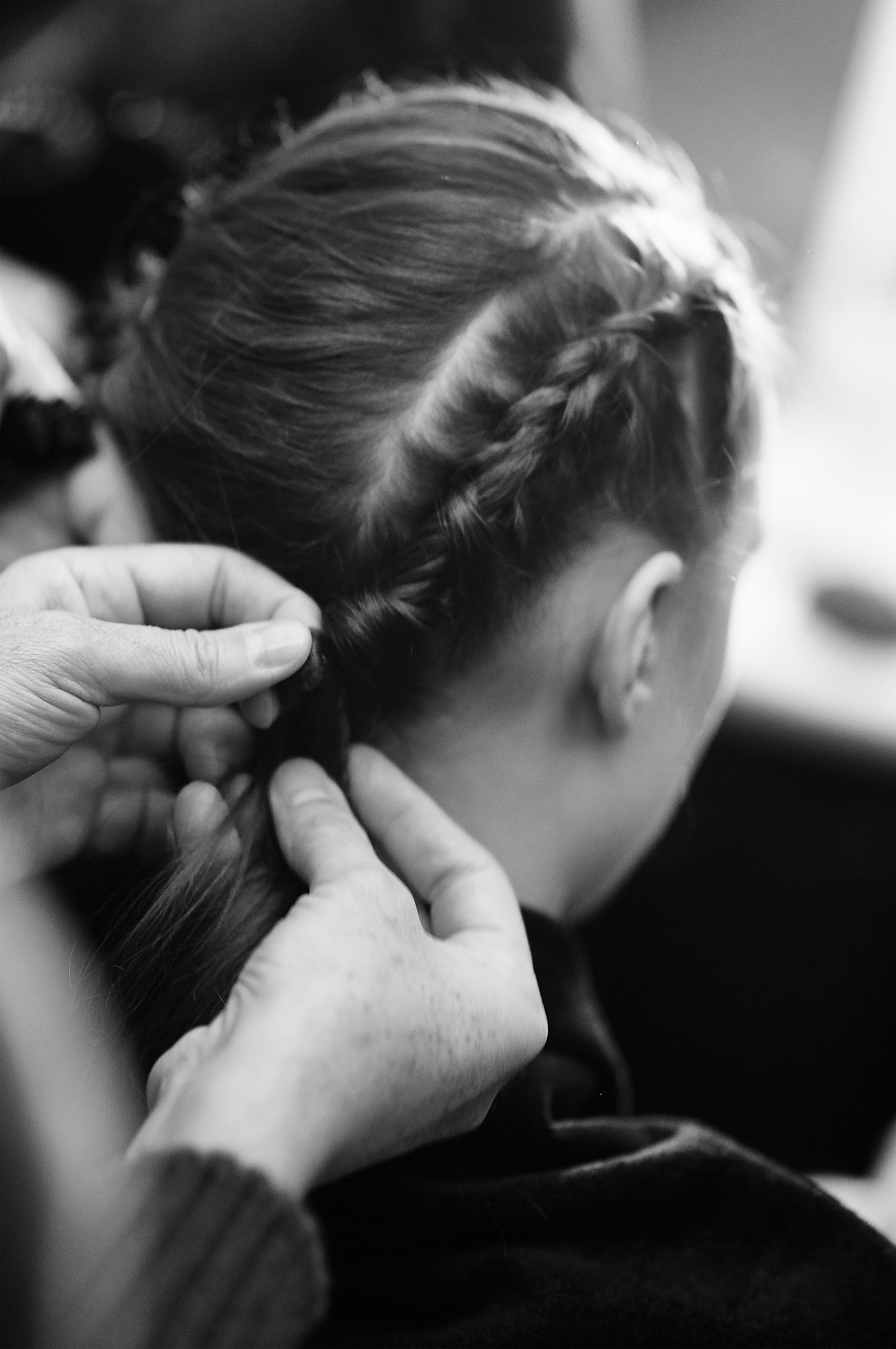 A stylist fixing a model's long, dark wavy hair into a tight braid 