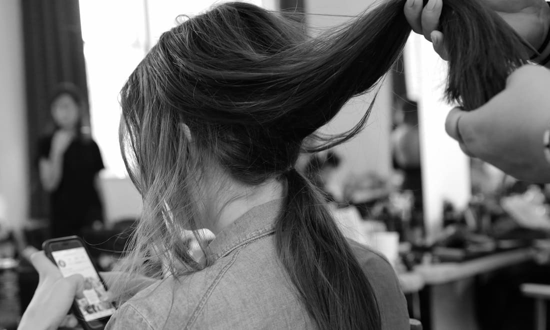 Un estilista sosteniendo un mechón grande de pelo de una modelo con sus manos