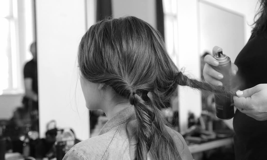 A stylist's hands applying hair spray to a section of a model's plaited hair.