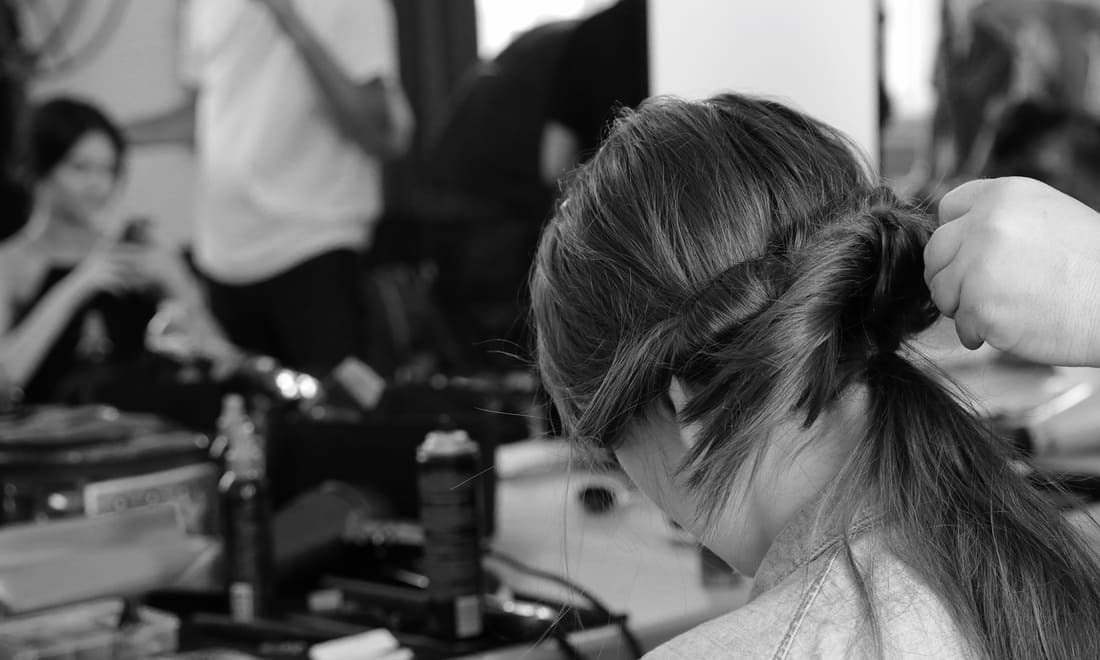 The hands of a stylist touching the back of a model's hair, fixing it into a thick plait.