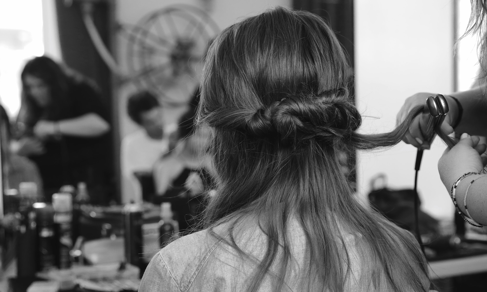 Model with a thick, loose plait and a stylist applying heat styling tongs to it