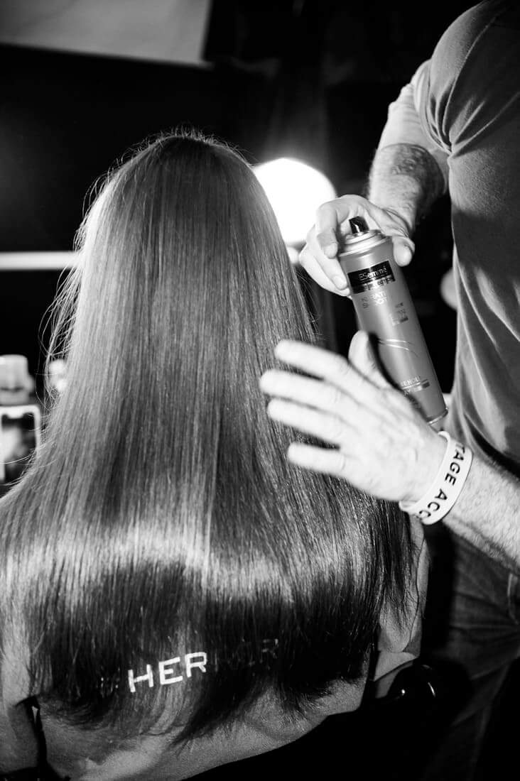A stylist applying spray to a model's hair backstage.