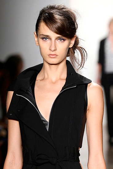 Una modelo luce un vestido negro con cierre y cuello alto y el pelo peinado hacia el lado