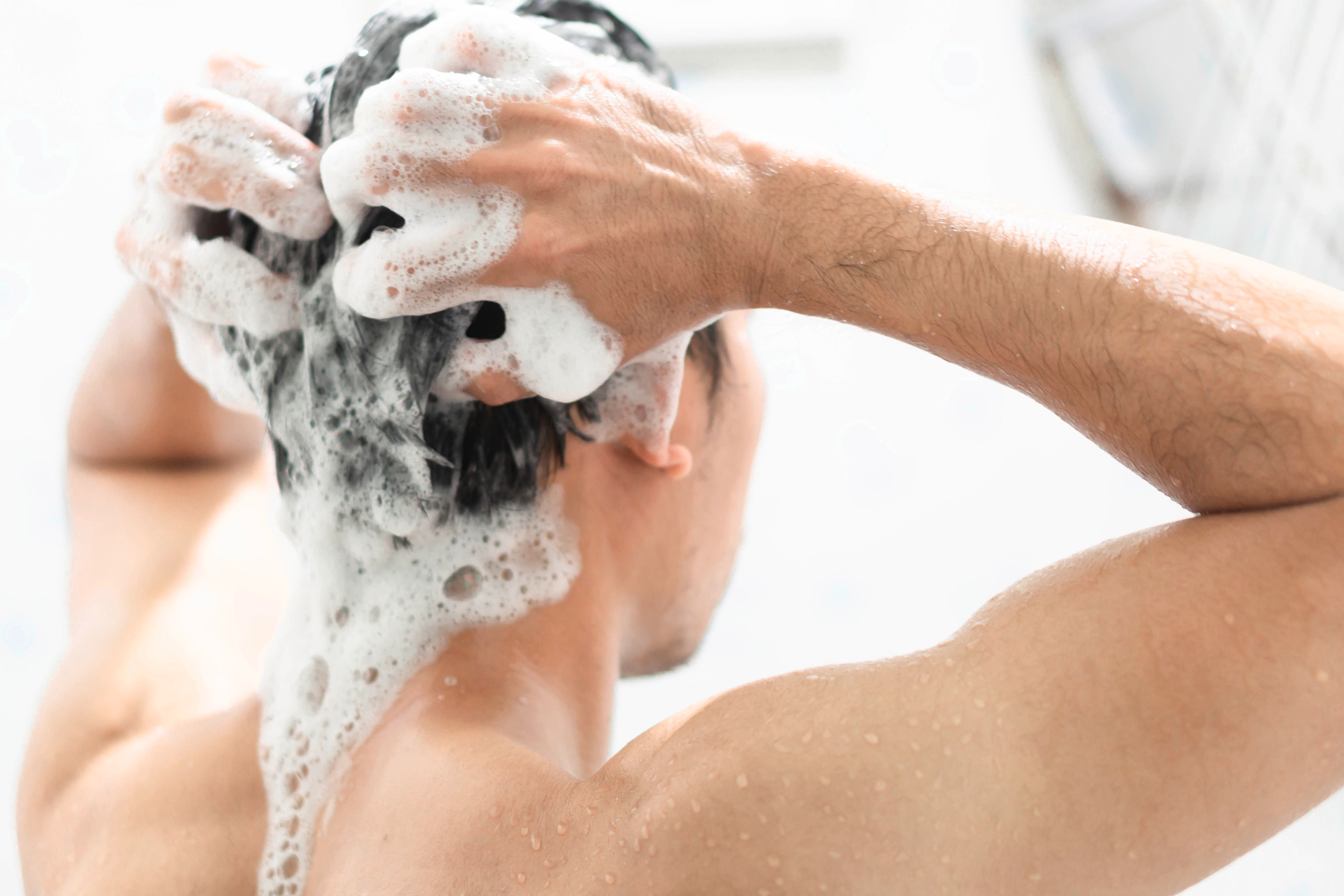 Young man washes his hair with shampoo.