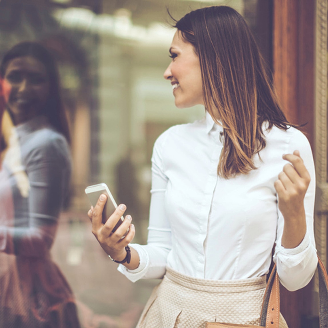 Mulher com cabelo com brilho liso loiro, olhando para um vidro e sorrindo.