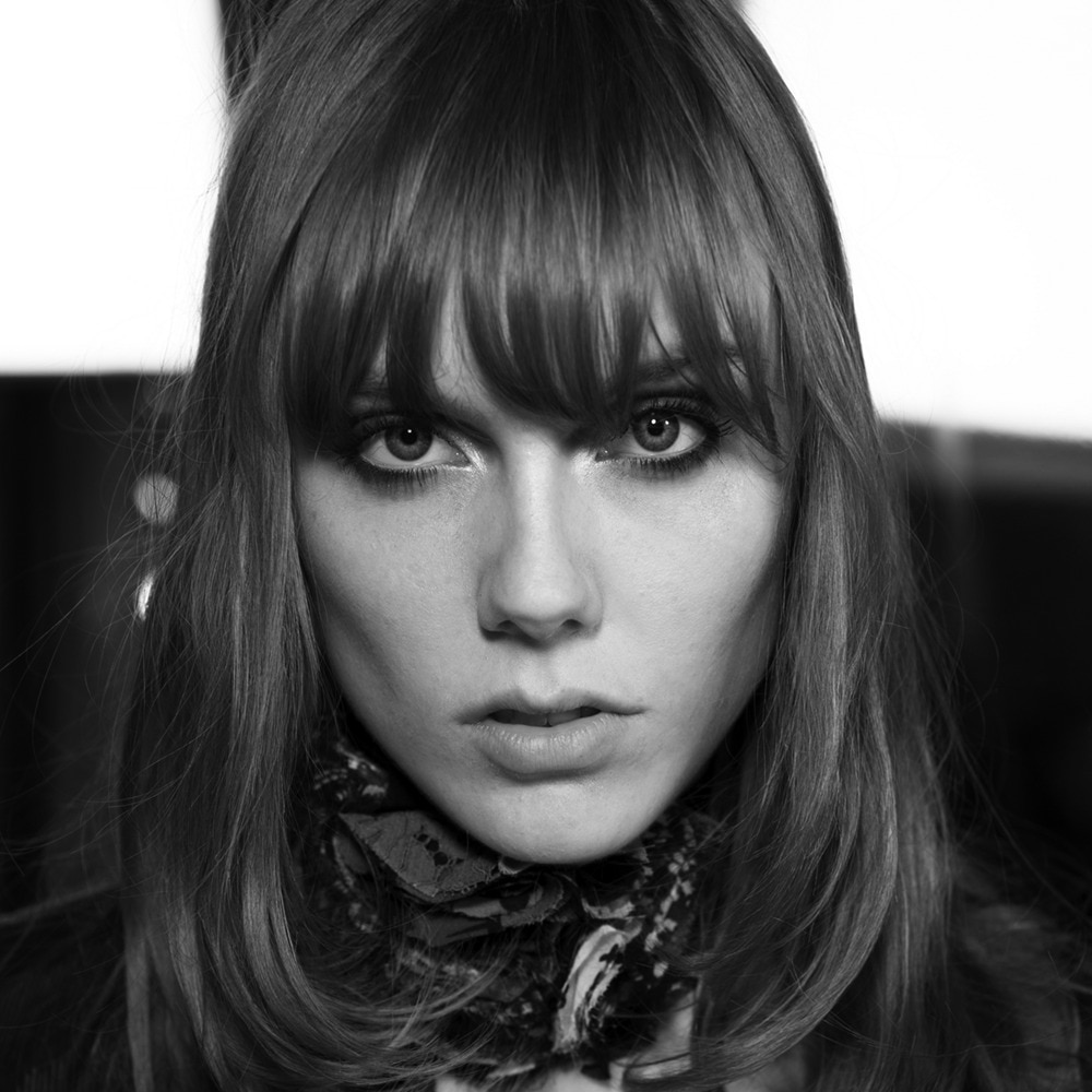 A model staring intensely at the camera with eyebrow-length brown bangs