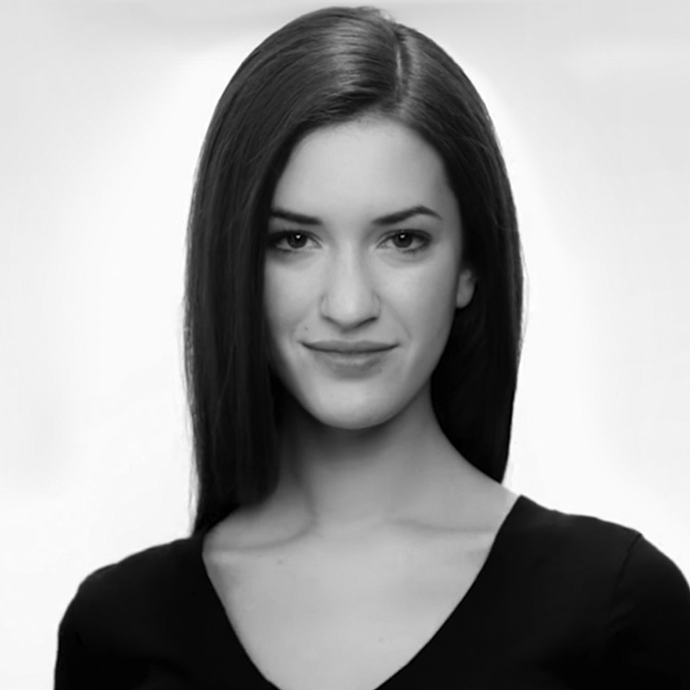 Una modelo sonriendo con el cabello castaño y raya, vistiendo un top negro con cuello de pico 