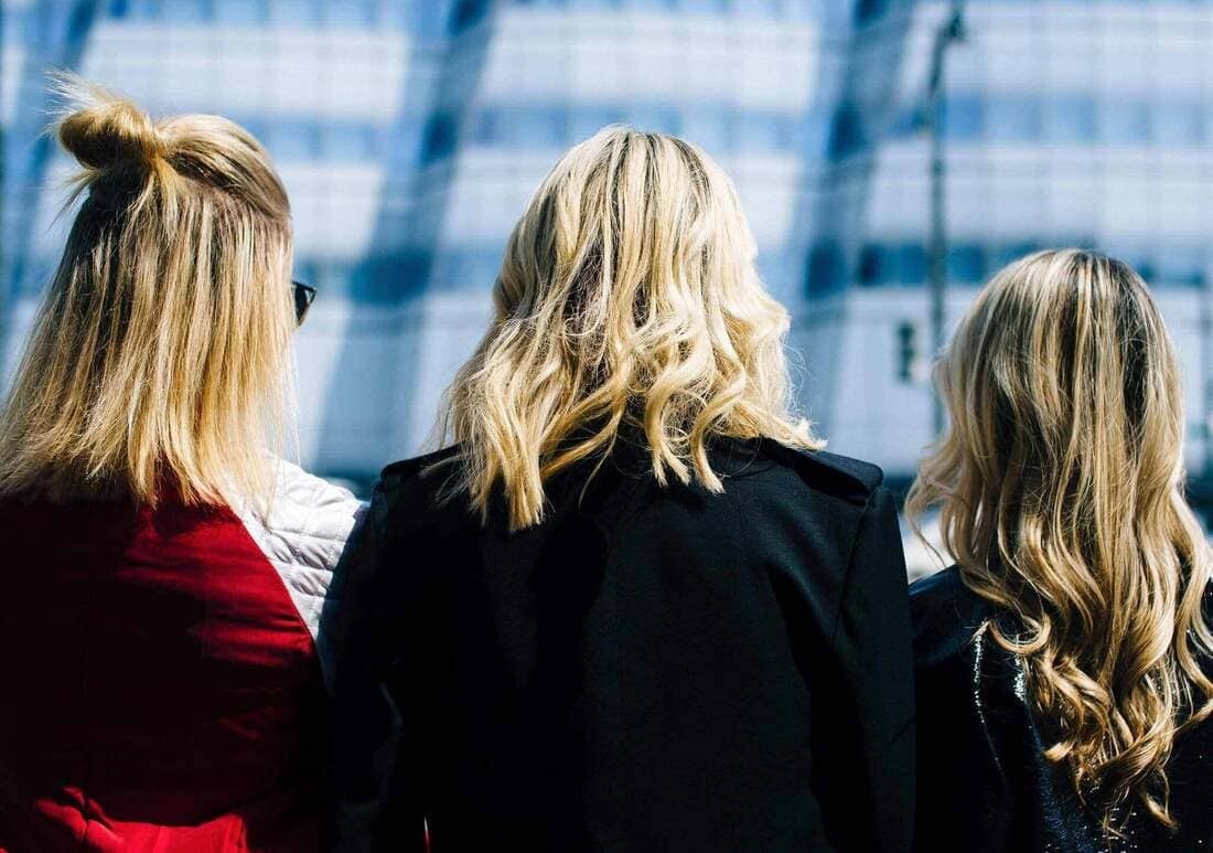 Three blonde women standing on a busy city street 