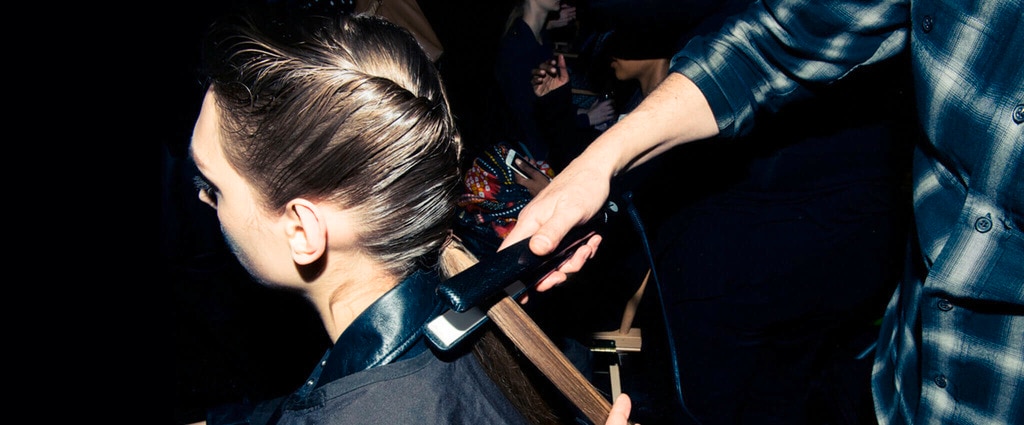 Detrás de escena de un desfile de modas, un estilista alisa el pelo castaño largo de una modelo.