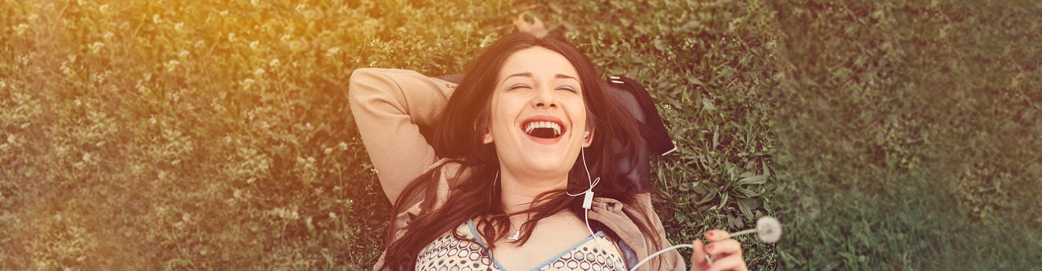 Woman with straight black hair, laying on the green grass with headphones
