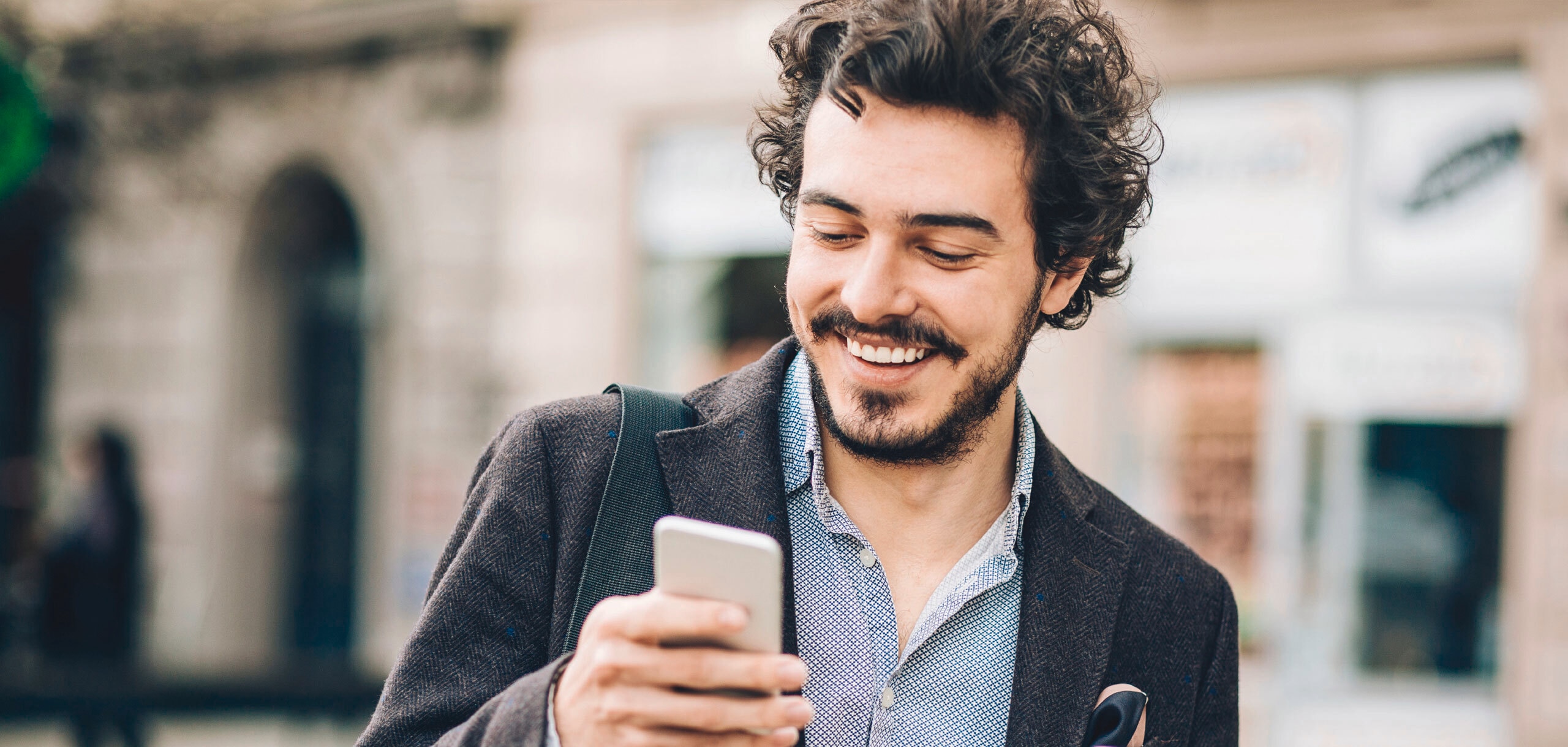 portrait d'un jeune homme souriant aux cheveux bouclés tenant une tasse de café et son téléphone portable