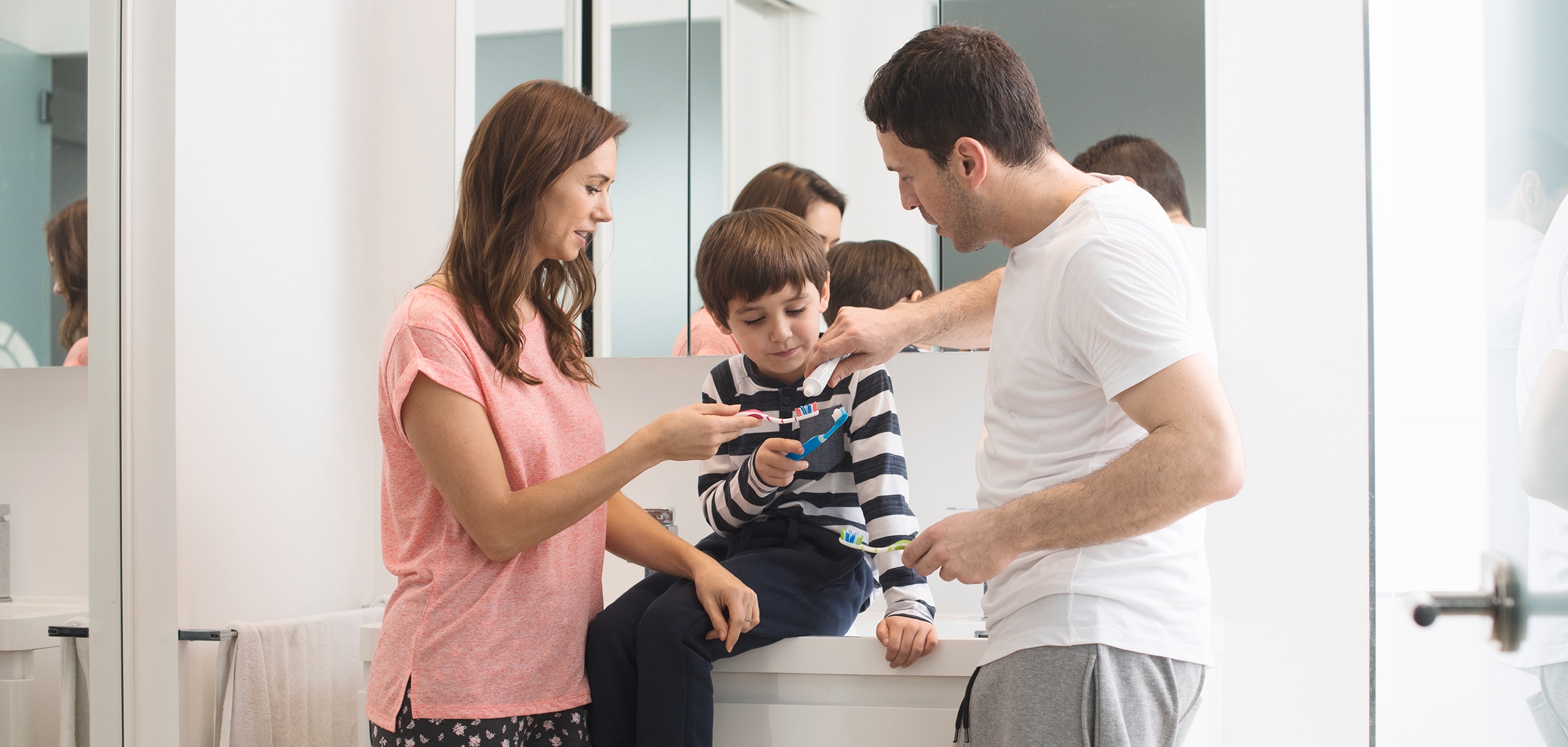 Dvaja rodičia pomáhajú svojmu dieťaťu čistiť si zuby pomocou Prodentu.