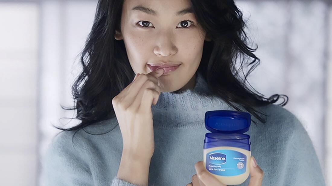 woman holding a vaseline pot and applying the product in her lips