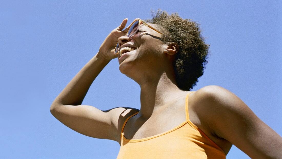 woman wearing sunglasses and smiling against blue sky