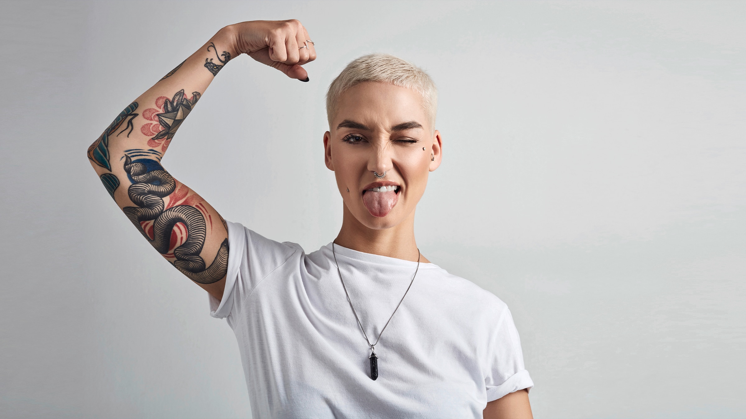 A person is shown flexing their arm. Tattoos are on the arm as the person is sticking their tongue out with one eye winced as well.