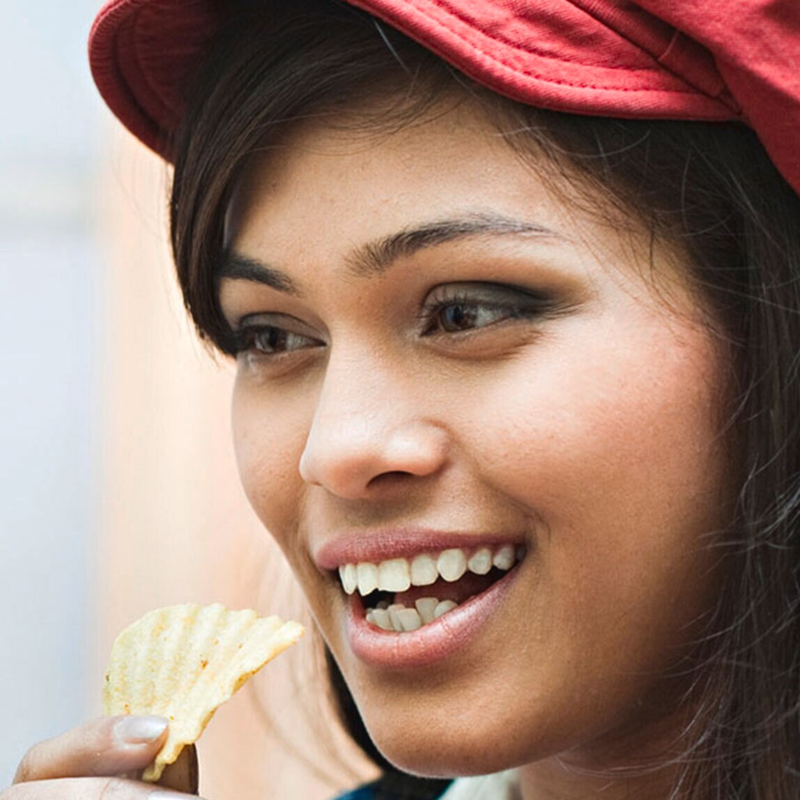 Close-up of a woman in a red cap eating crisps.
