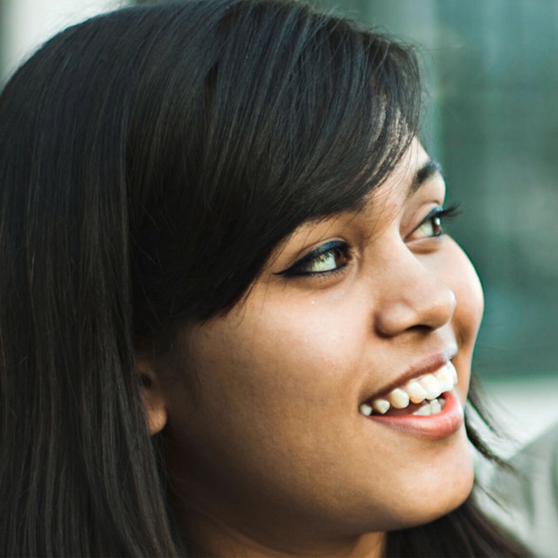 Side view of a smiling woman's face. Her hair is thick, straight and black. 