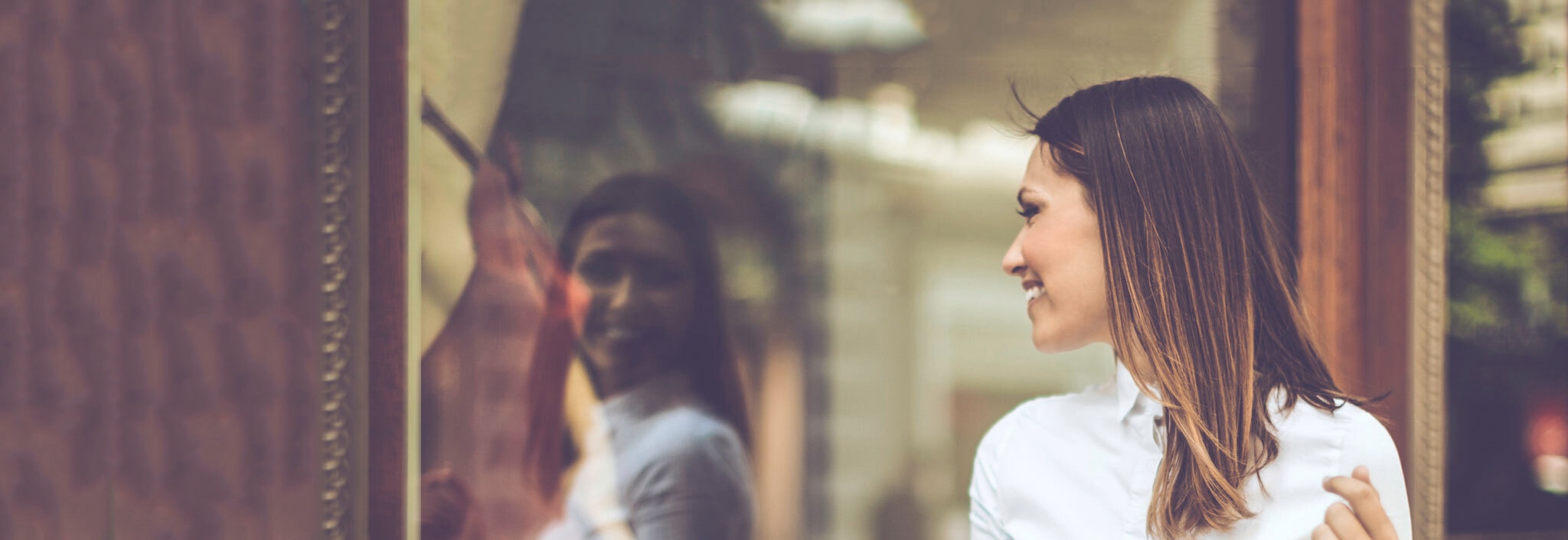 Mulher com cabelo com brilho liso loiro, olhando para um vidro e sorrindo.