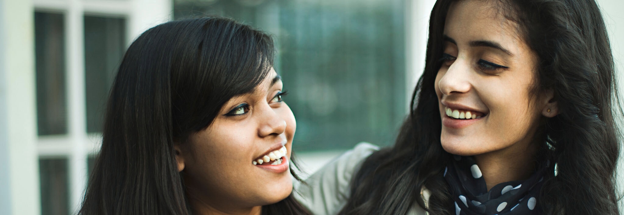 Close up of two women with thick black hair looking at each other mid-conversation