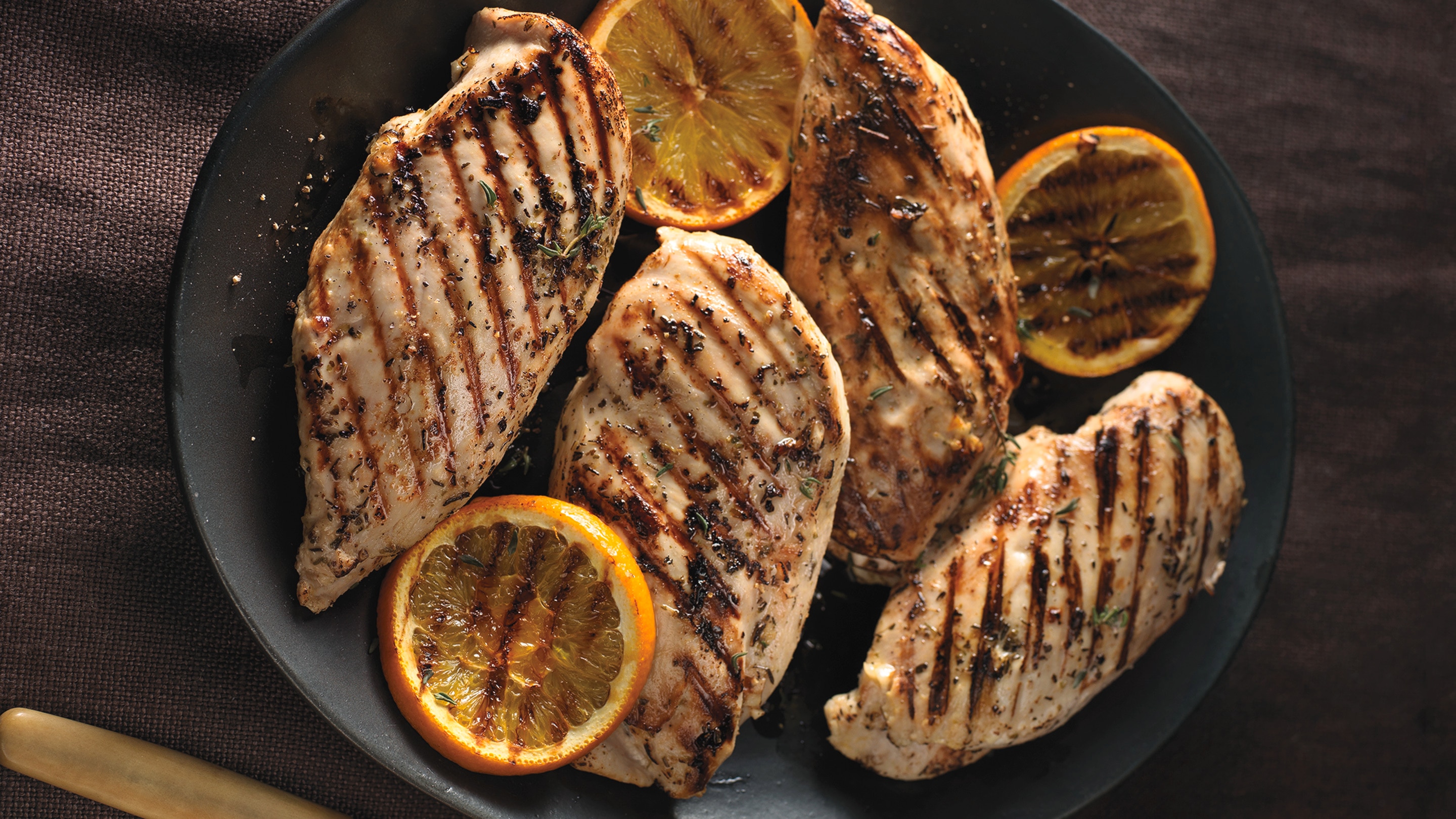 Grilled chicken breasts with grilled orange garnish on a black plate