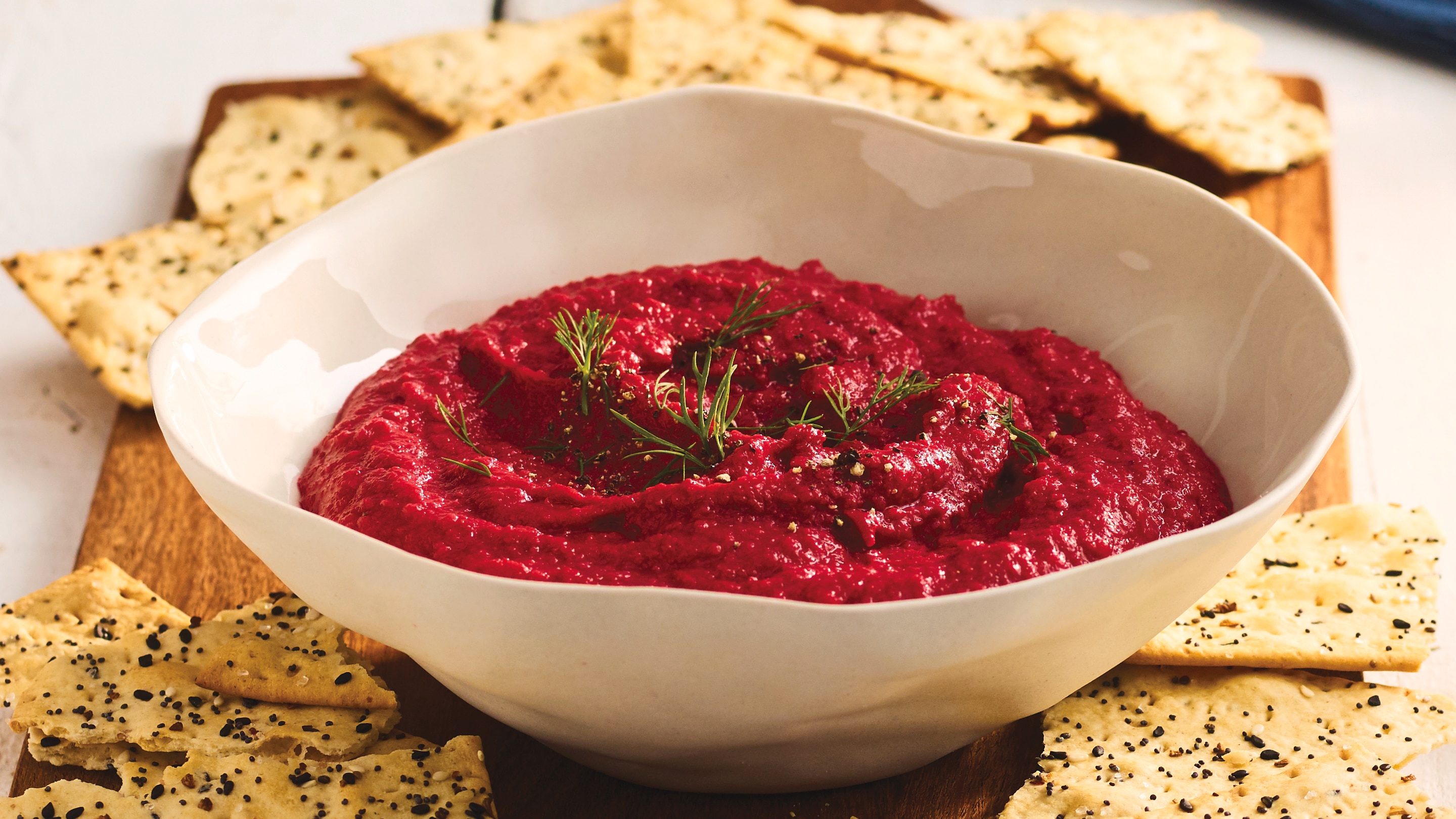 Purple beet hummus in a bowl surrounded by multigrain crackers