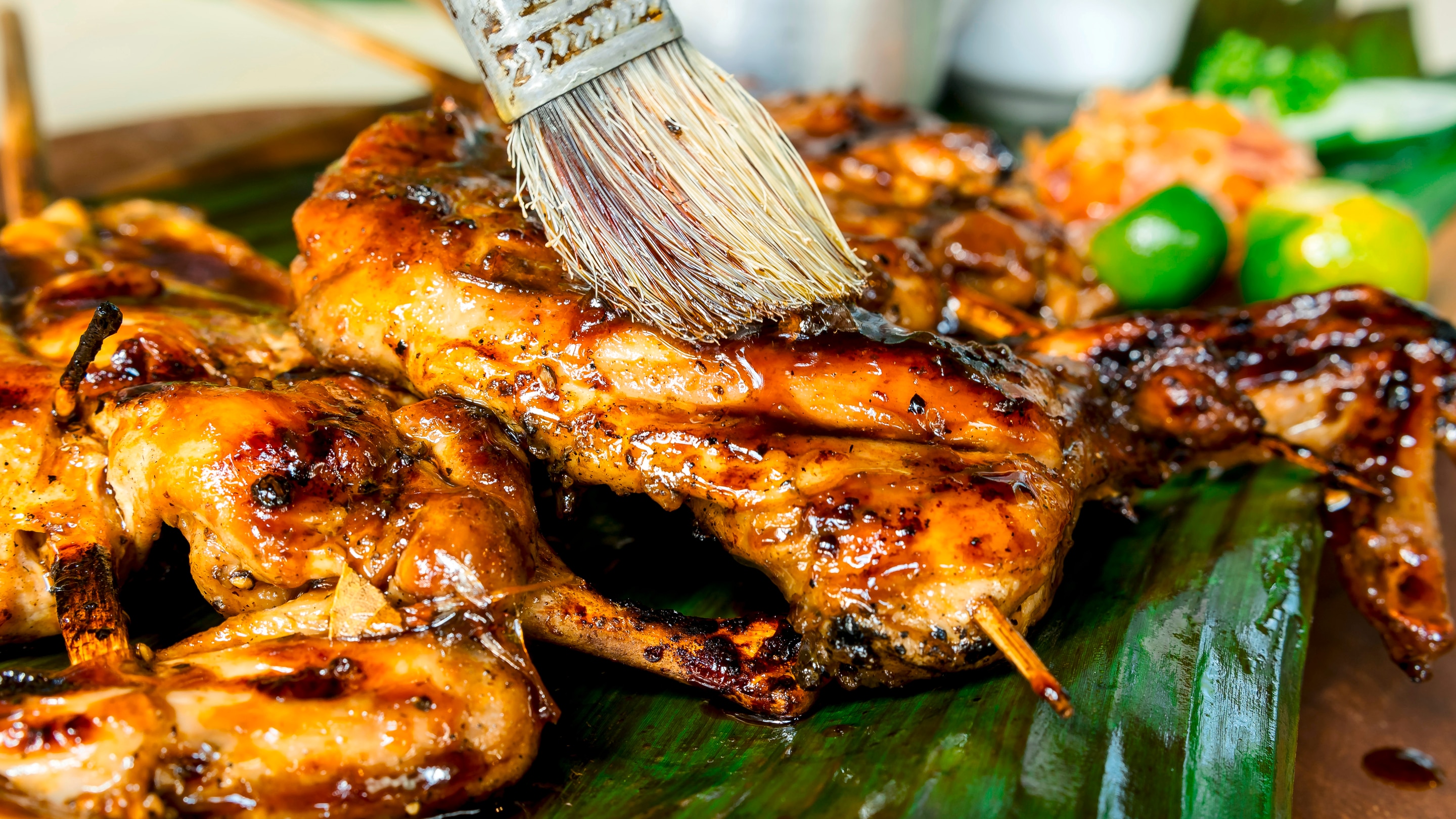 Grilled chicken pieces on a banana leaf get final basting before it is served