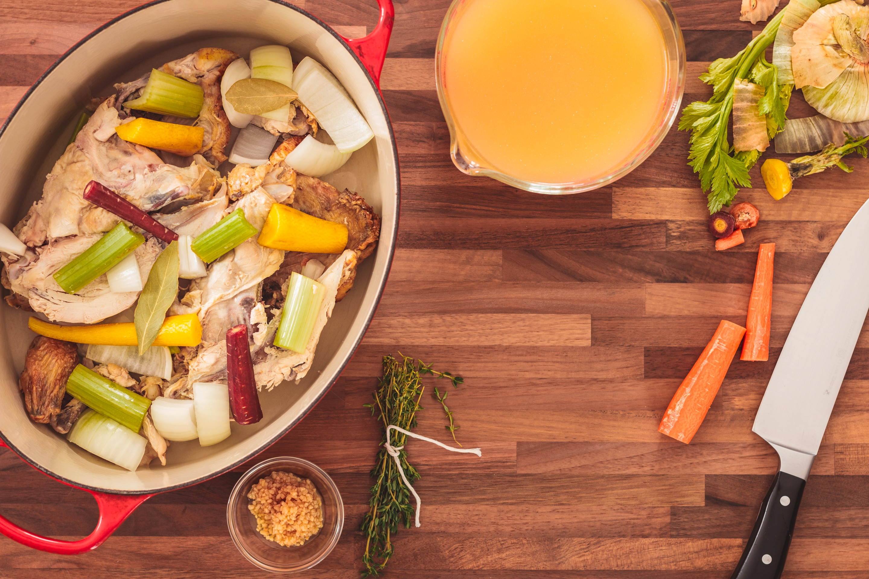 Roasted chicken sits in a pot with chopped celery, carrots, onions, and spices