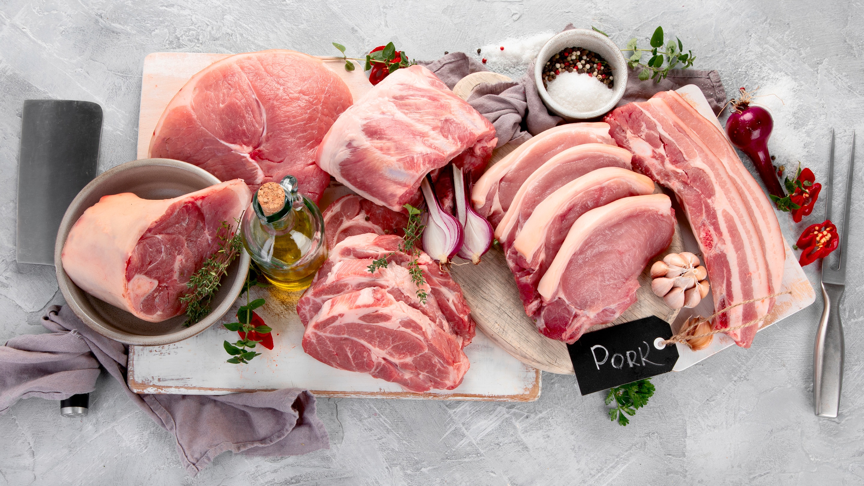 An assortment of different cuts of pork with a bottle of olive oil and herbs as decorations