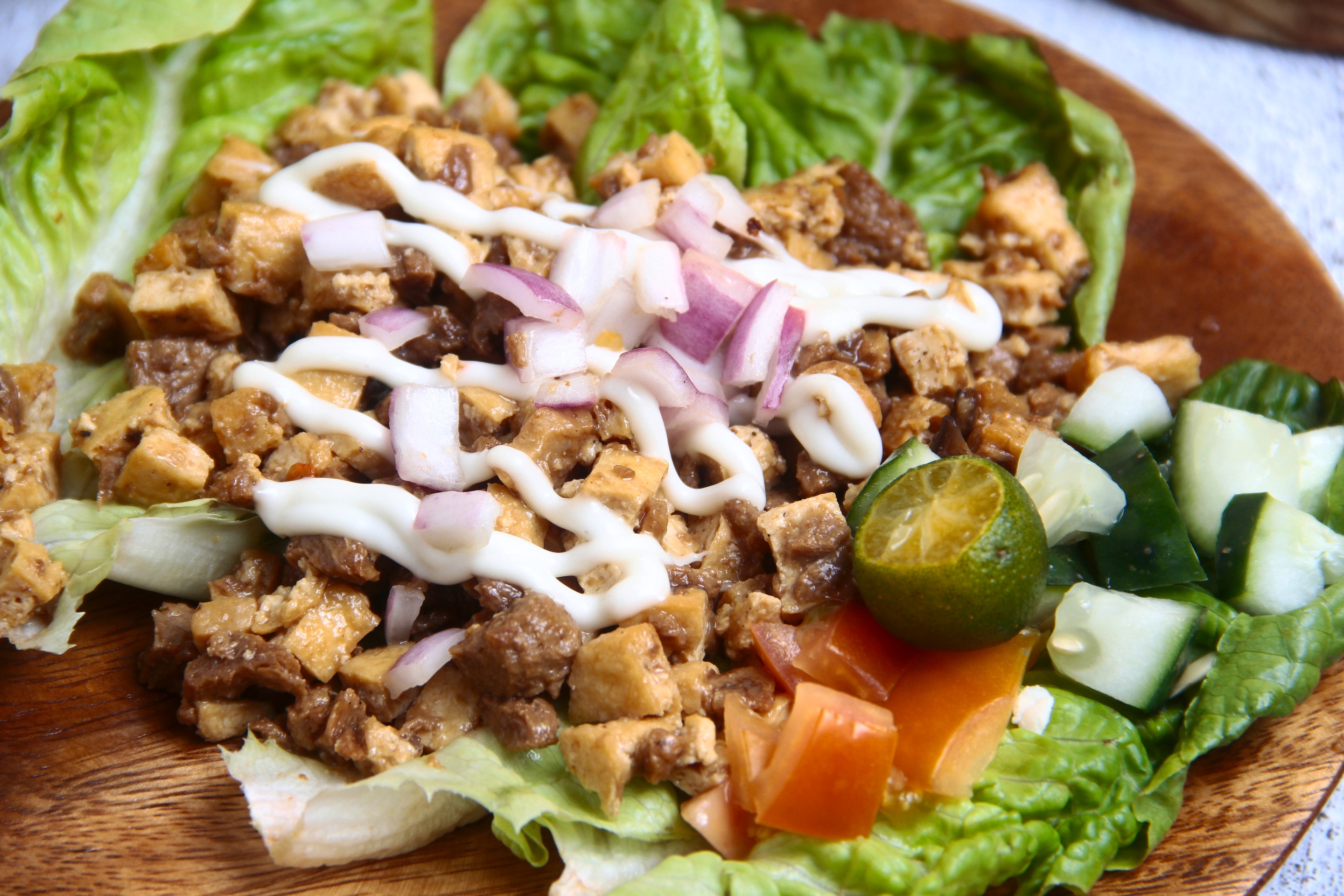 A plate of Tofu Sisig on a piece of lettuce with mayonnaise drizzles