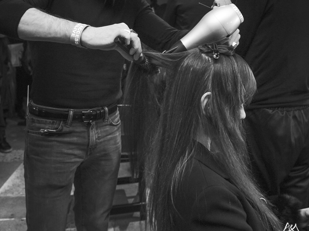 Two stylists working on a model's hair with combs and straighteners 