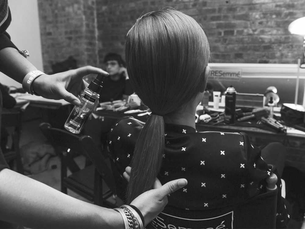 Las manos de un estilista tocando la parte de atrás del cabello de una modelo y peinándolo con una trenza gruesa.