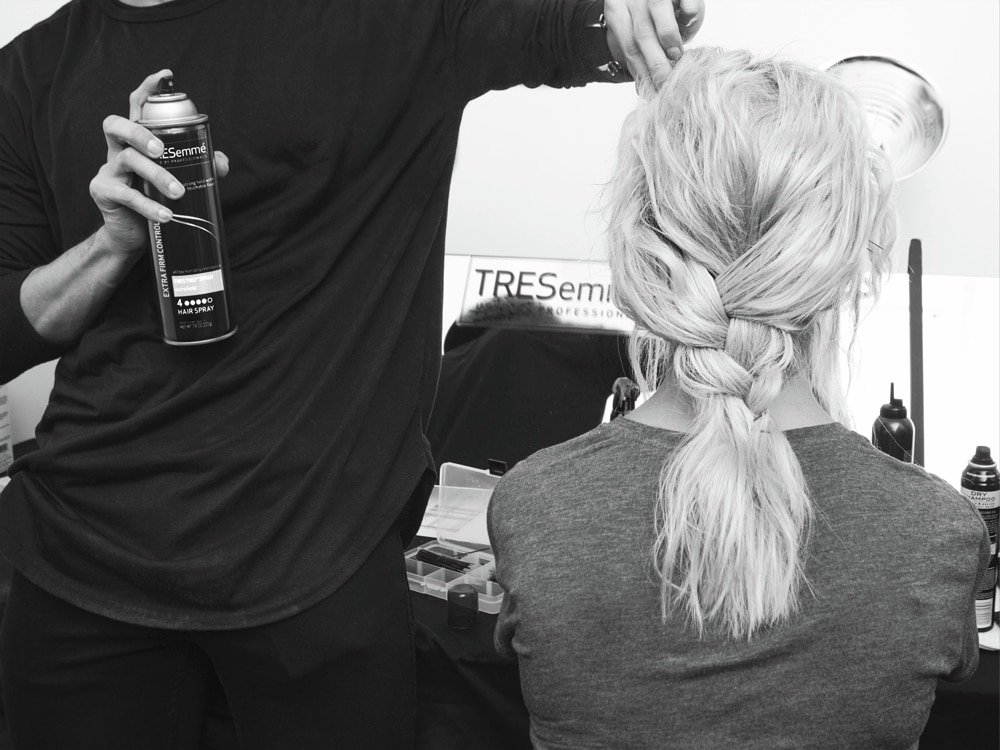 Un estilista uniendo dos secciones del cabello de una modelo en la parte de atrás de su cabeza.