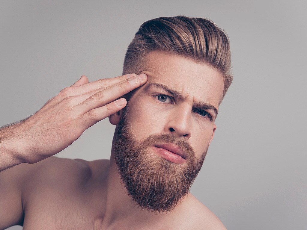 Hombre con pelo liso y look hacia atrás tocando su frente 