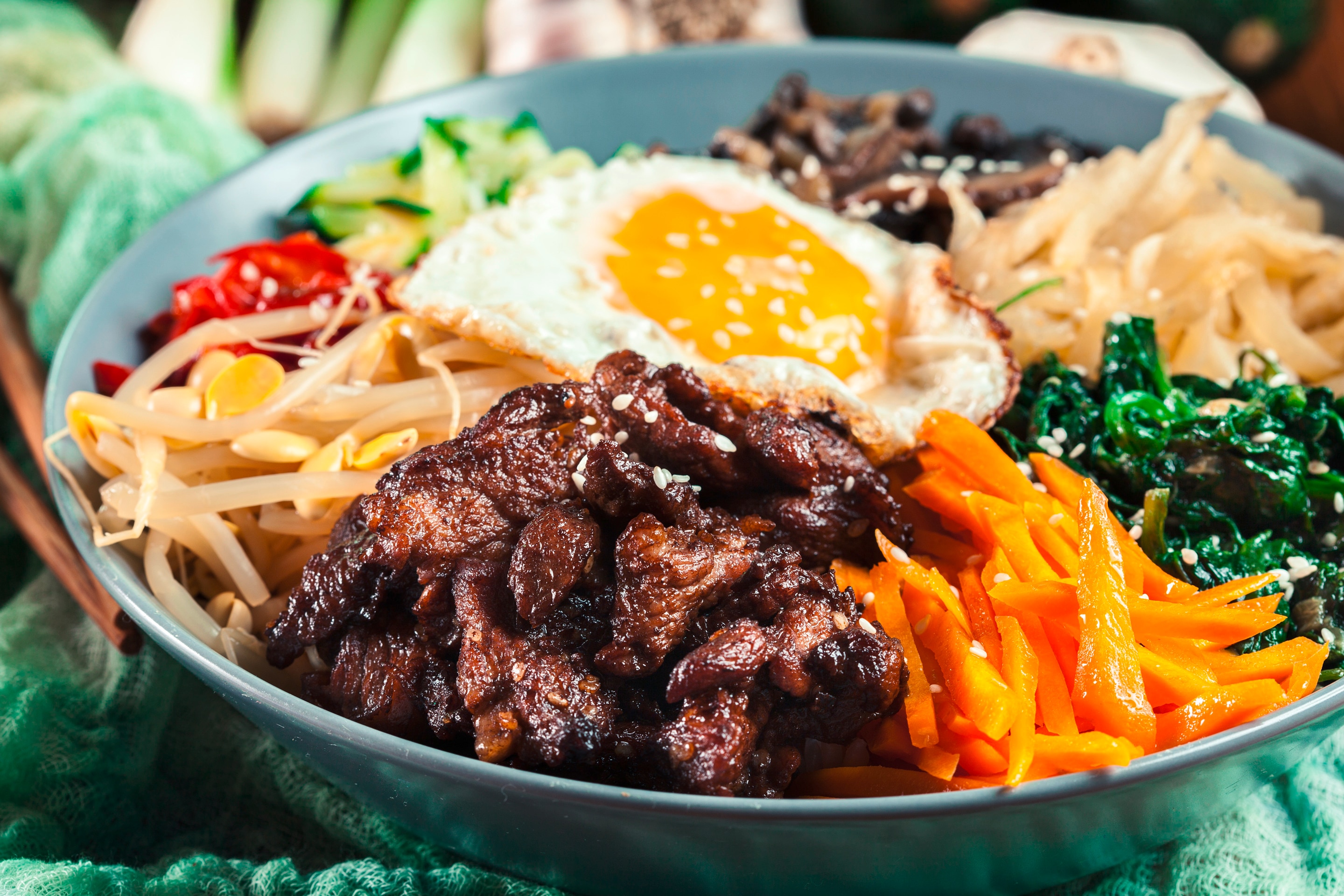 Bibimbap with slices of beef, carrot, kangkong, togue, cucumber, mushroom, and chili in a bowl of rice with a sunny-side up egg on top
